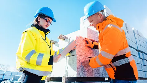 To byggearbeidere med verneutstyr samarbeider om isolasjonsmaterialer på byggeplass